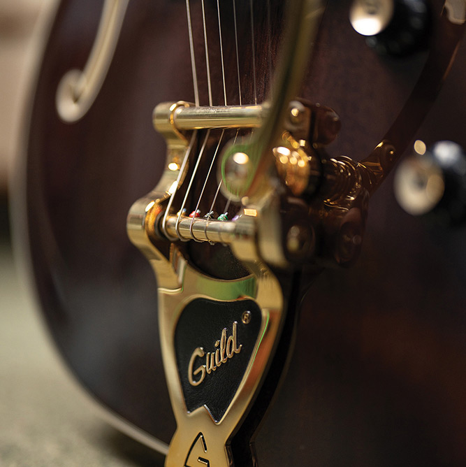 Close-up of the gold Guild Vibrato tailpiece on a Starfire Custom DC GVT GH, showing the engraved Guild script.