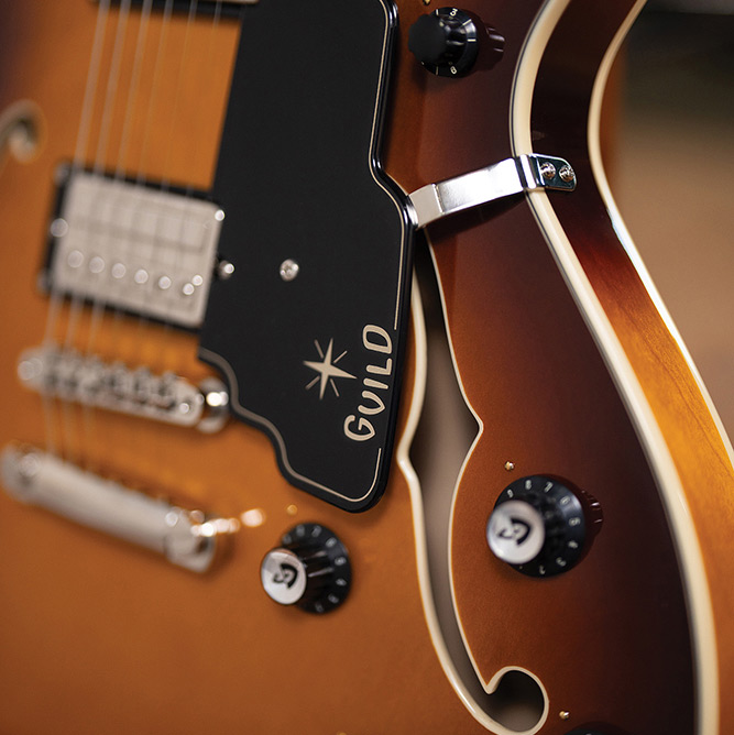 Close-up of the upper cutaway horn on a Starfire Deluxe DC Sweet Tea, showing the pickguard with Guild logo, tailpiece, and control knobs.
