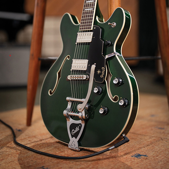 Full view of a Starfire Deluxe DC GVT Emerald Green leaning against a stool, showing the double-cutaway body, pickguard, and pickups.