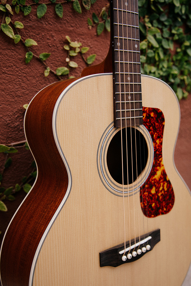 Close-up of Jumbo Junior Mahogany body in front of a wall with vines