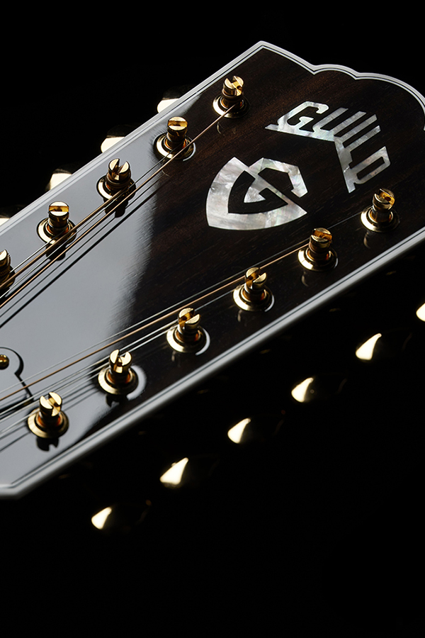 Close-up of F-512E guitar headstock featuring the Guild logo and gold tuning pegs.