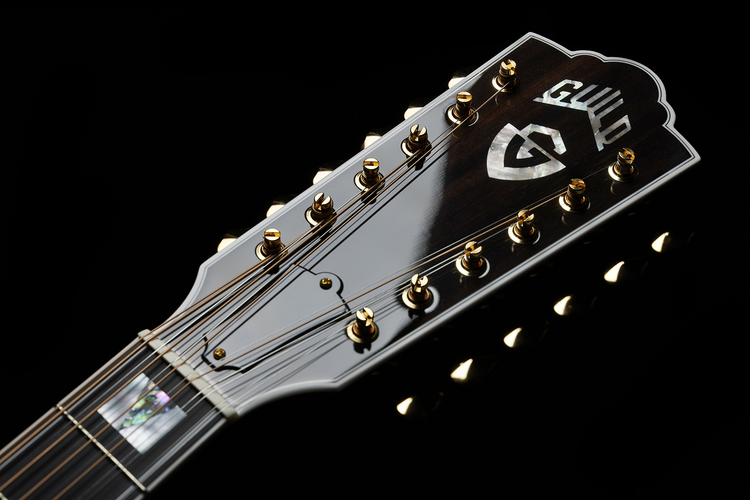 Close-up of F-512E guitar headstock featuring the Guild logo and gold tuning pegs.
