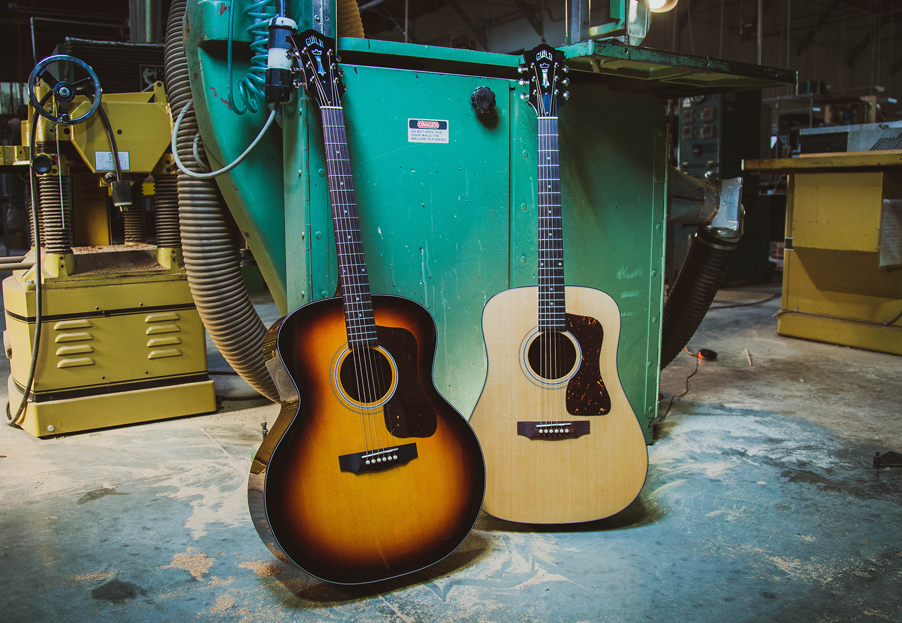F-40 Natural and Antique Burst acoustic guitars positioned in guitar workshop with machinery in the background.