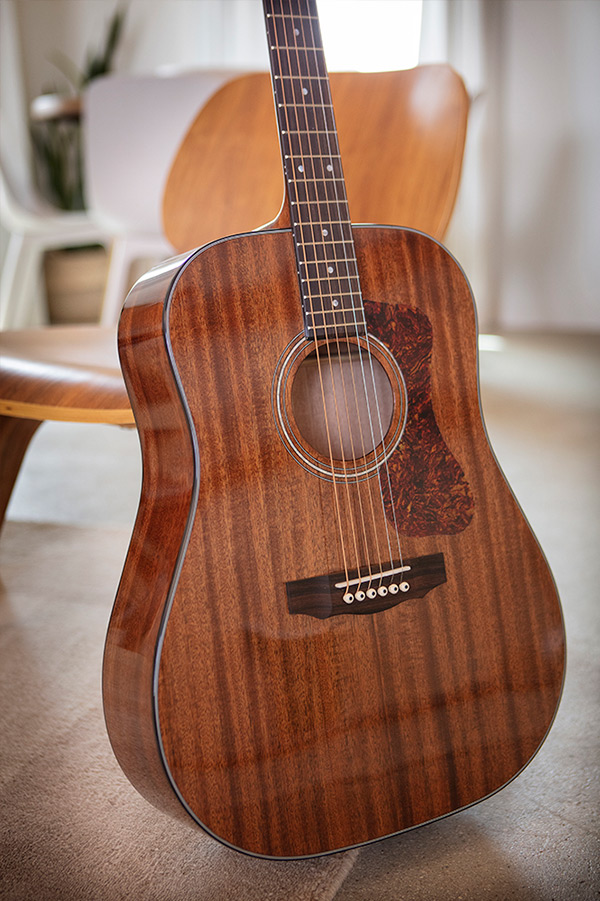 D-150 acoustic guitar leaning against a wood chair in a cozy room thumbnail
