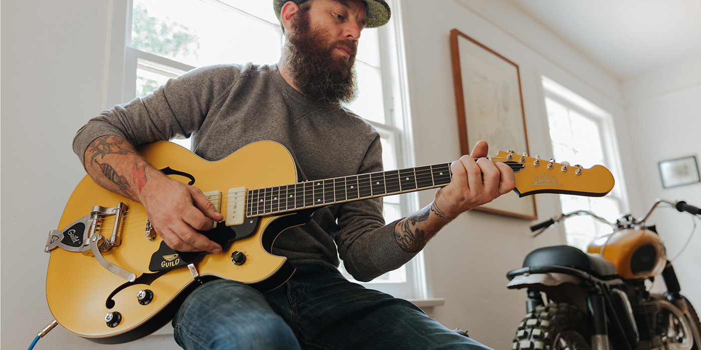 Man playing a Starfire I Jet90 Satin Gold in his loft by a motorcycle