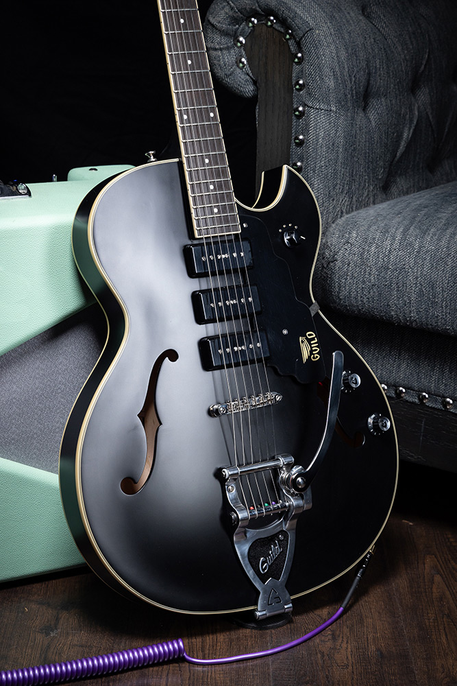 Starfire I Jet90 Satin Black electric guitar leaning against an amp by a gray sofa
