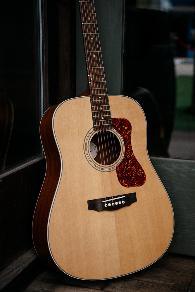Close up D-240E Natural learning against glass doors showing pickguard, soundhole, bridge, and Solid Sitka Spruce top