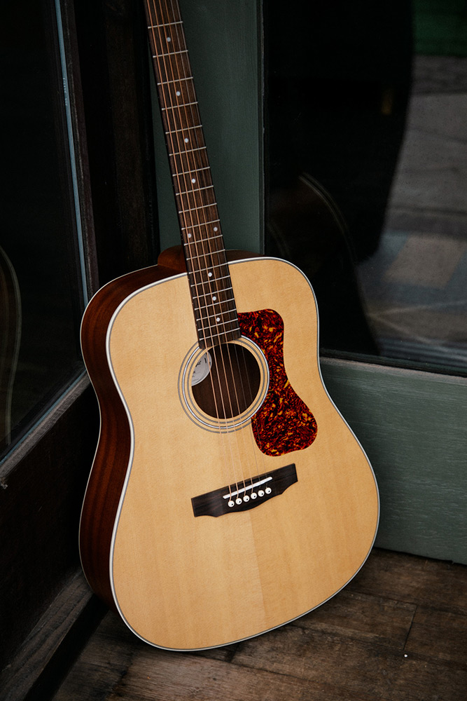 Close up D-240E Natural learning against glass doors showing pickguard, soundhole, bridge, and Solid Sitka Spruce top