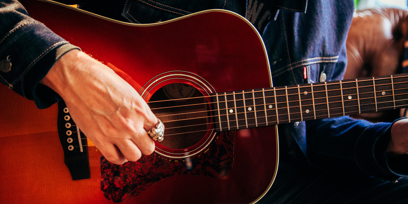 Close up of a person playing the D-140 acoustic guitar while sitting on a couch