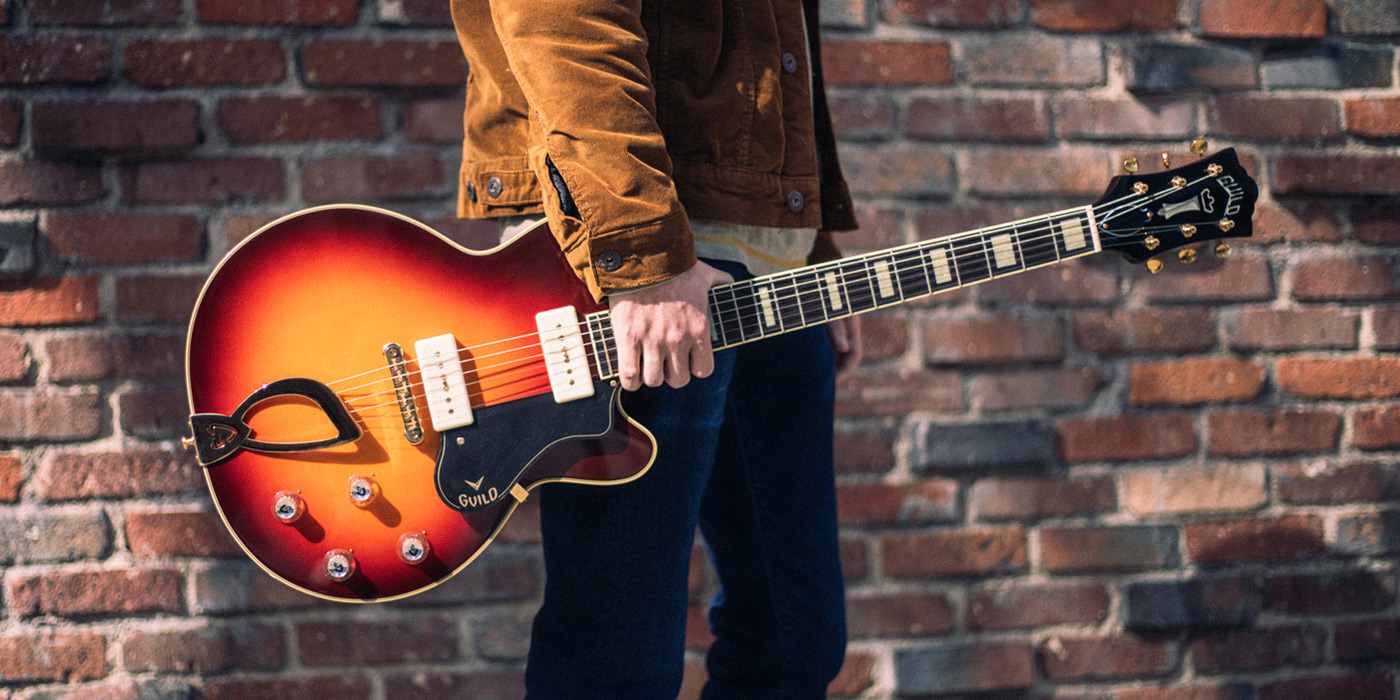 M-75 Aristocrat Antique Sunburst guitar being held in front of a brick wall