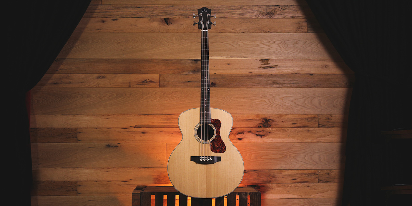 B-240E Natural acoustic guitar lit from behind in front of a wood wall