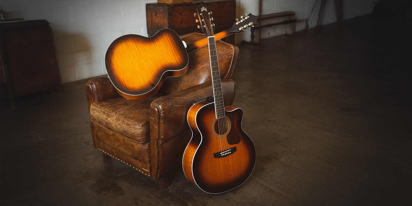 Two F-250CE Deluxe Archback Antique Burst acoustic guitars on a brown leather chair. One front facing and one back facing.