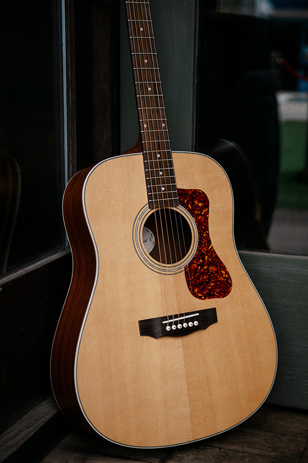 Close up D-240E Natural learning against glass doors showing pickguard, soundhole, bridge, and Solid Sitka Spruce top