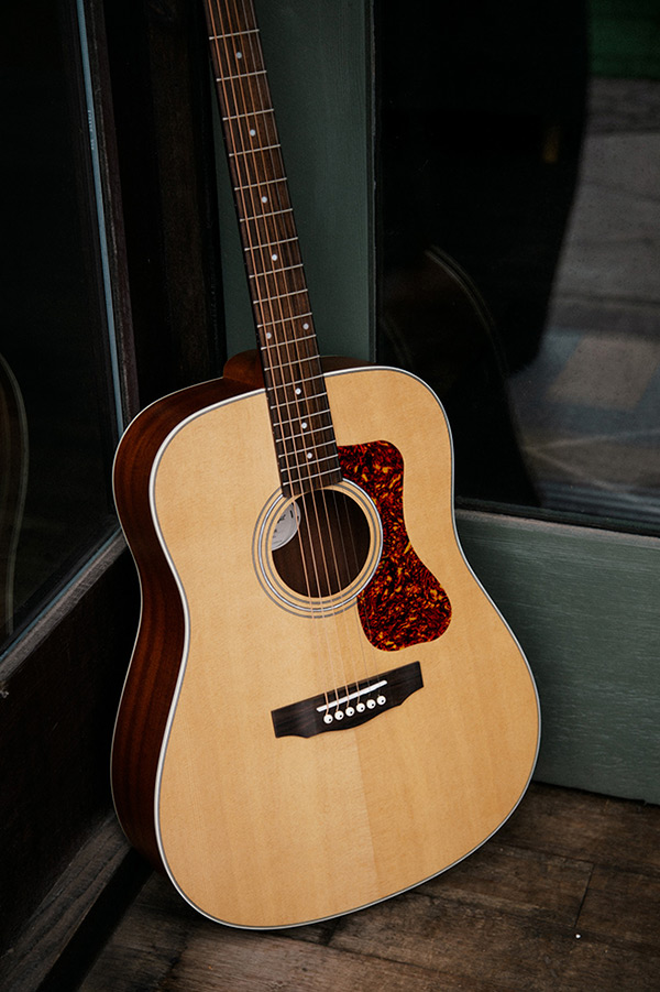 Close up D-240E Natural learning against glass doors showing pickguard, soundhole, bridge, and Solid Sitka Spruce top
