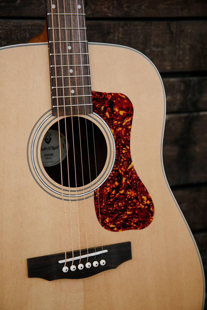 Close up D-240E Natural body showing pickguard, soundhole, bridge, and Solid Sitka Spruce top