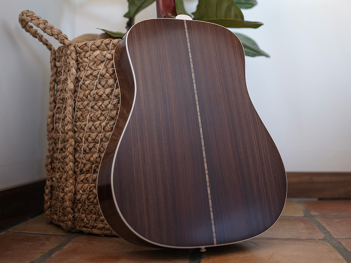 Back view of D-50 Standard Antique Burst leaning against a wicker pot with plant
