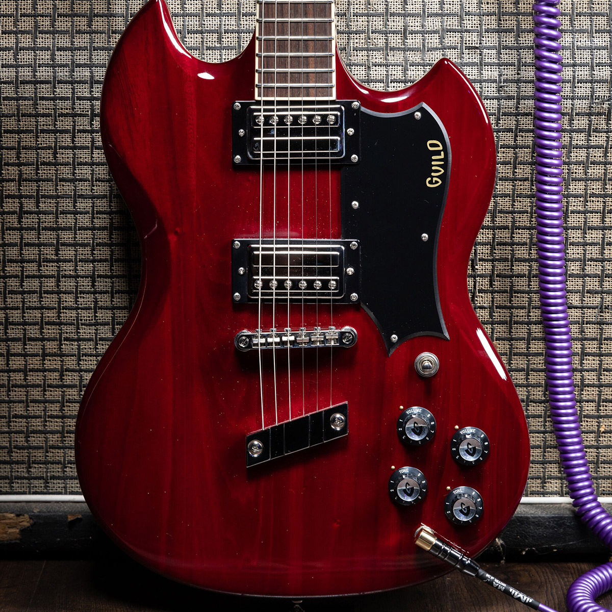 Close-up of Polara Deluxe Cherry Red body leaning against adn plugged into an amp with purple coil cord