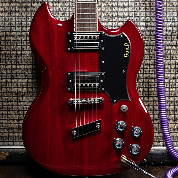 View of Polara Deluxe Cherry Red leaning on an amp with a purple coiled plug thumb