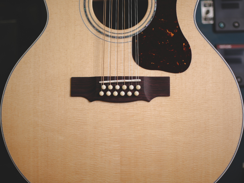 Close-up of F-512 acoustic guitar's body, showcasing its wood grain, pickguard, and bridge with white bridge pins.