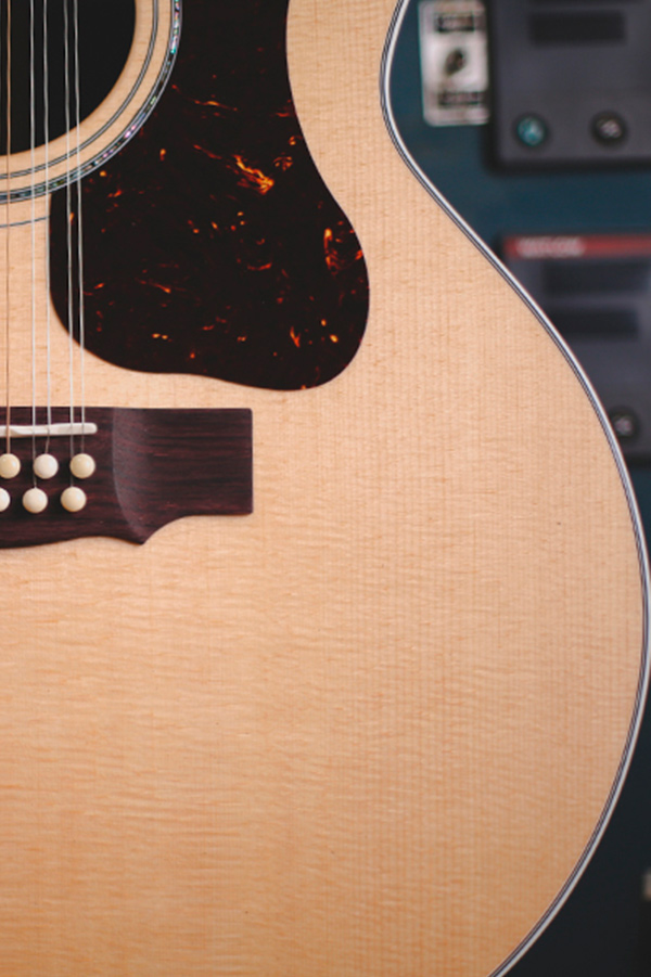Close-up of F-512 acoustic guitar's body, showcasing its wood grain, pickguard, and bridge with white bridge pins.