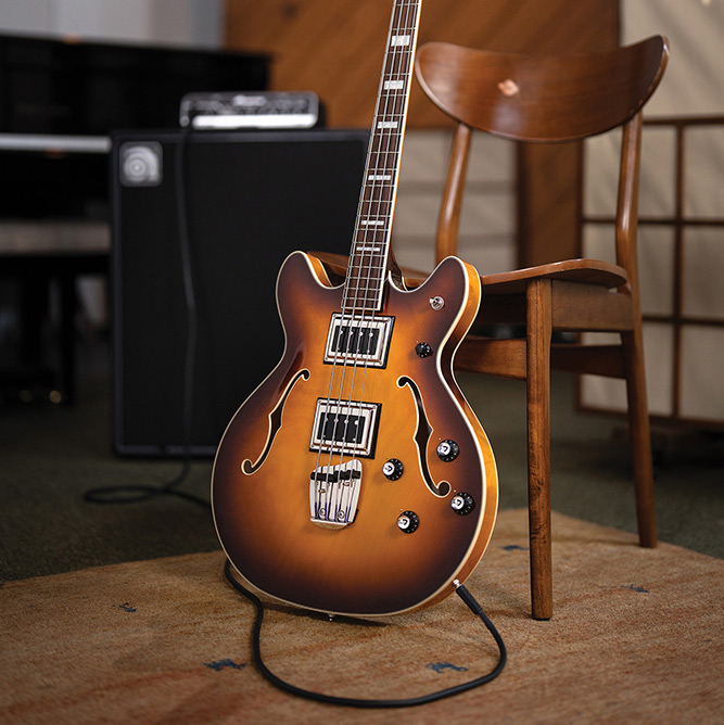 Full view of a Starfire Deluxe Bass Sweet Tea leaning on a chair, showing the double-cutaway semi-hollow body and Sweet Tea sunburst finish.