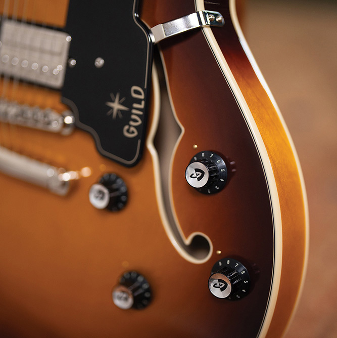 Close-up of the lower body bout on a Starfire Deluxe DC Sweet Tea, showing the pickguard with Guild logo, tailpiece, control knobs, and F-hole.