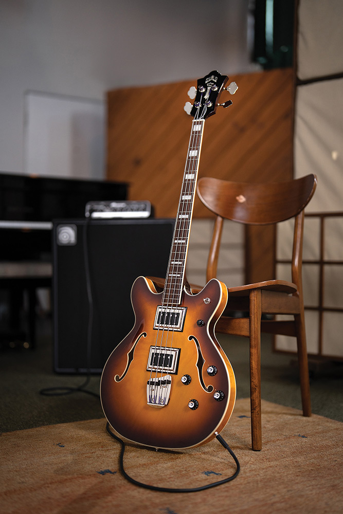 Full view of a Starfire Deluxe Bass Sweet Tea leaning on a chair, showing the double-cutaway semi-hollow body and Sweet Tea sunburst finish.