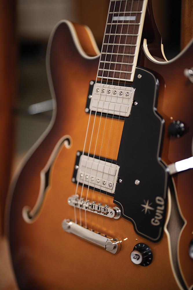 Close-up of the neck meeting the body on a Starfire Deluxe DC Sweet Tea, showing the pickguard with Guild logo, both HB-2+ pickups, and stop tailpiece.
