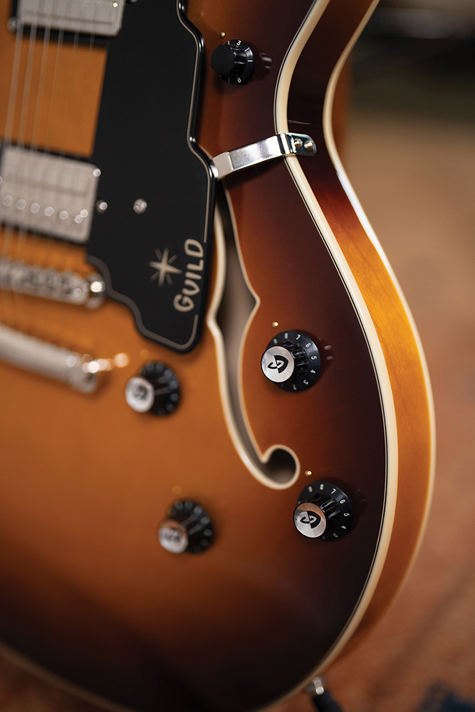 Close-up of the lower body bout on a Starfire Deluxe DC Sweet Tea, showing the pickguard with Guild logo, tailpiece, control knobs, and F-hole.