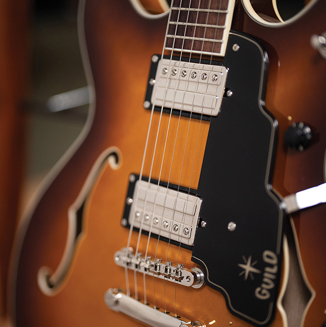 Close-up of the neck meeting the body on a Starfire Deluxe DC Sweet Tea, showing the pickguard with Guild logo, both HB-2+ pickups, and stop tailpiece.