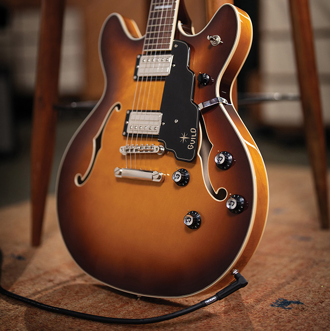 Full view of a Starfire Deluxe DC Sweet Tea leaning against a stool, showing the double-cutaway body, pickguard, pickups, and Sweet Tea sunburst finish.