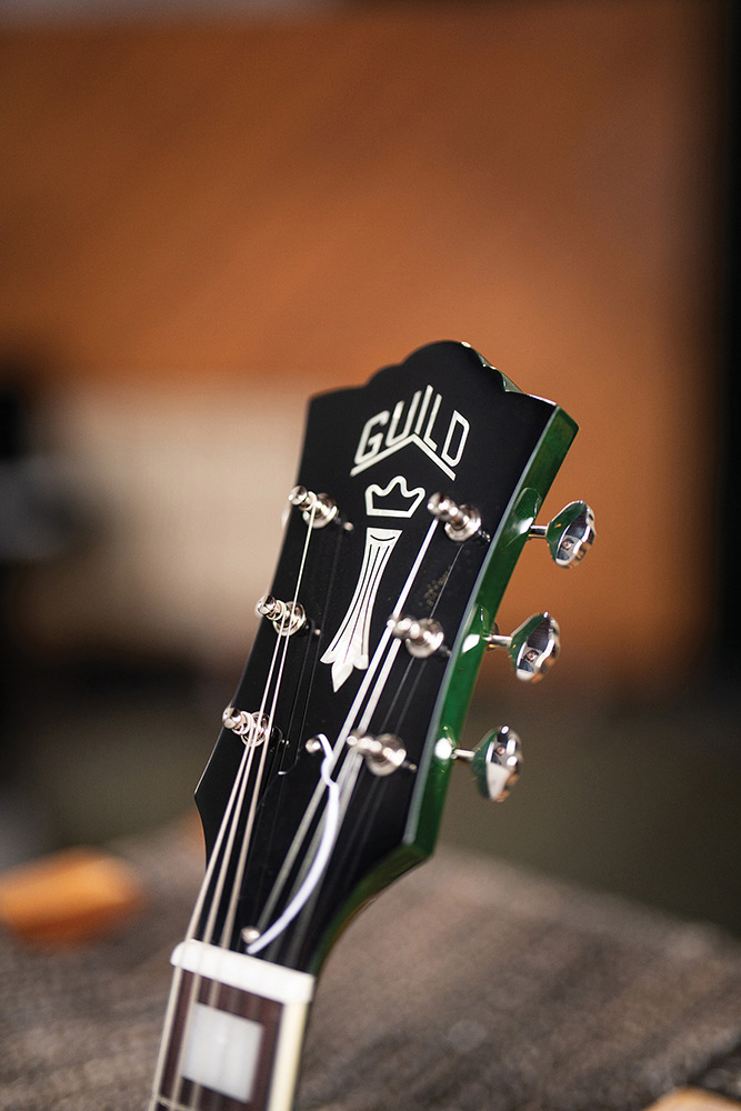 Close-up of the headstock on a Starfire Deluxe DC GVT Emerald Green, showing the Guild Peak logo, Chesterfield inlay, and Grover open-gear tuners.