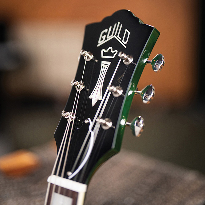 Close-up of the headstock on a Starfire Deluxe DC GVT Emerald Green, showing the Guild Peak logo, Chesterfield inlay, and Grover open-gear tuners.