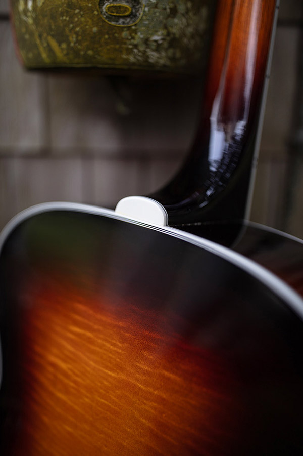 Close-up of F-55E Maple guitar's back neck and body, showcasing a glossy finish with warm, gradient colors. A rustic background is slightly blurred.