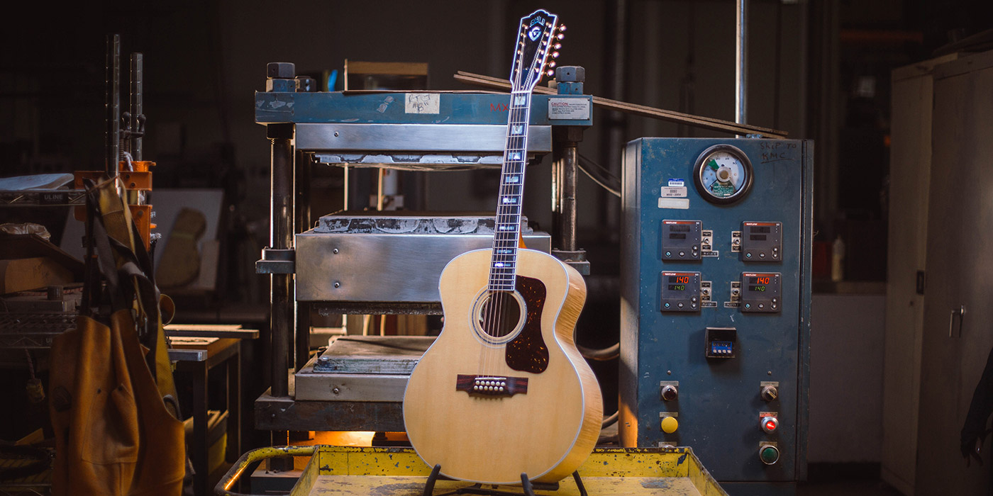 F-512 Maple Blonde acoustic guitar leaning against machinery in guitar factory