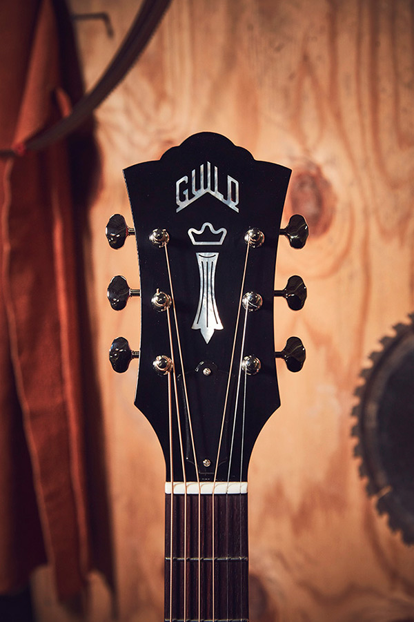 Close-up of D-40 guitar headstock featuring the Guild logo and tuning pegs, set against a wooden background.