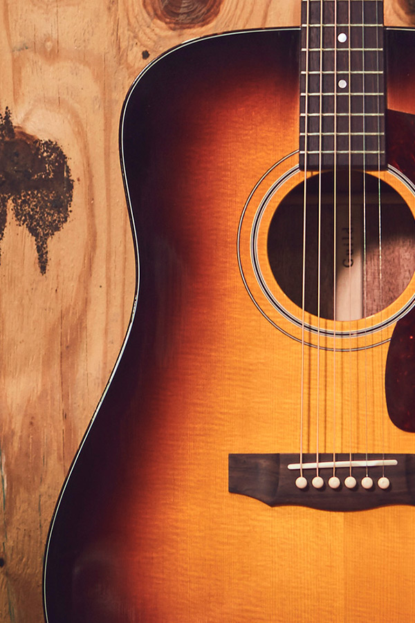 Close-up of D-40 acoustic guitar against a wooden background, showcasing its curves and strings.