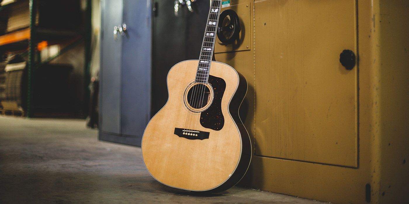 F-55 acoustic guitar leans against a yellow cabinet in guitar warehouse setting, with shelves and boxes in the background.