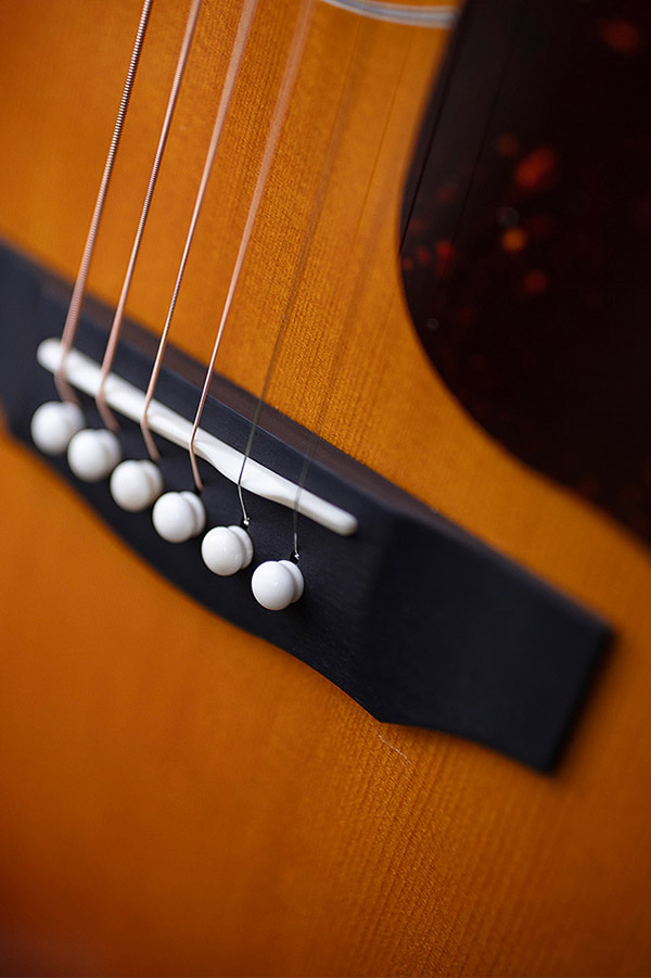 Close-up of F-55E Maple acoustic guitar's bridge and strings, showcasing the wooden texture and white bridge pins.