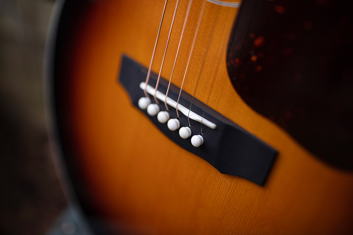 Close-up of F-55E Maple acoustic guitar's bridge and strings, showcasing the wooden texture and white bridge pins.