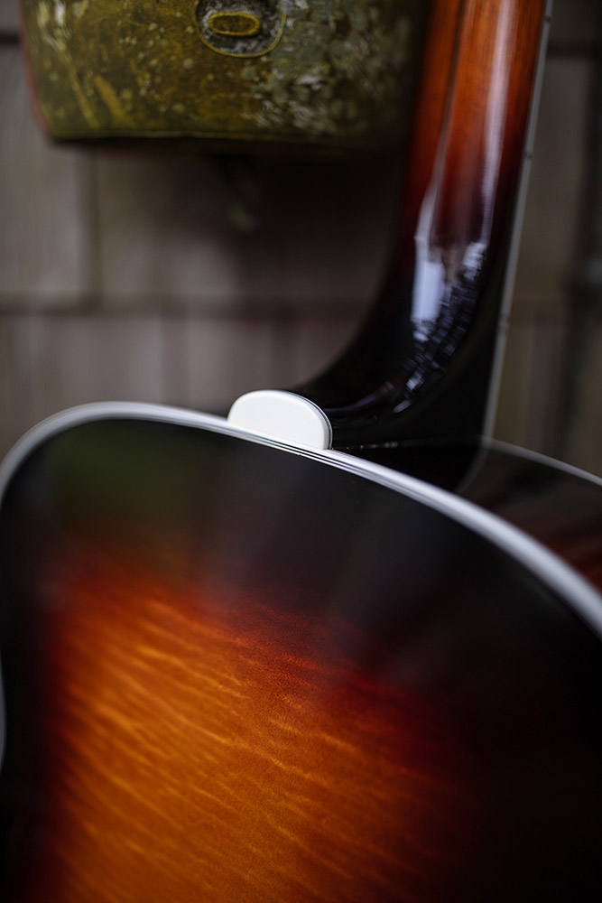 Close-up of F-55E Maple guitar's back neck and body, showcasing a glossy finish with warm, gradient colors. A rustic background is slightly blurred.