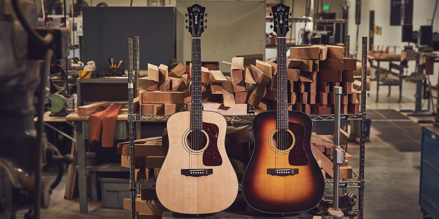 D-40 Natural and Antique Sunburst acoustic guitars leaning against a shelf in guitar workshop, surrounded by stacks of wood blocks.
