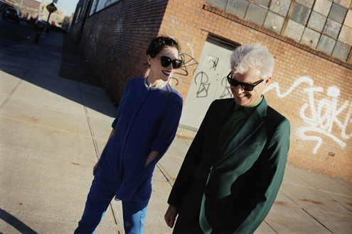 David Byrne et St. Vincent marchant dans une rue en passant devant un bâtiment avec des graffitis.